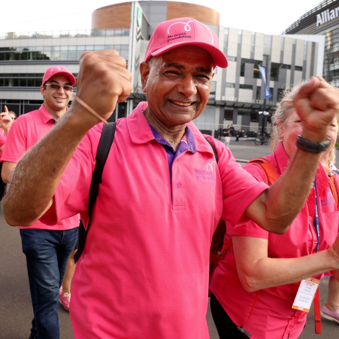 People wearing pink McGrath Foundation clothing participate in a fundraising walk outside a stadium.