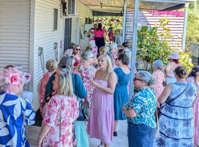 Guests socialising outdoors before or during the event, gathered along a covered veranda decorated with pink bunting.