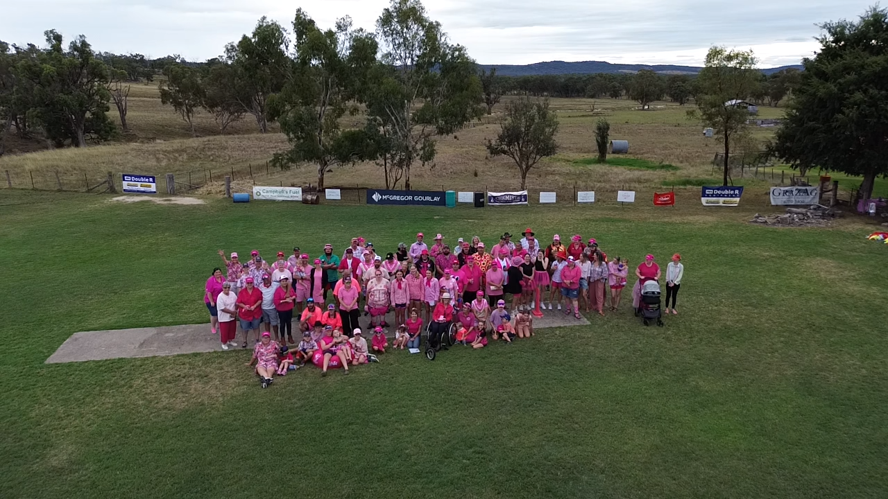 Aerial view of a large group of community members wearing pink gathered on a cricket field during a Pink Stumps Day fundraising event