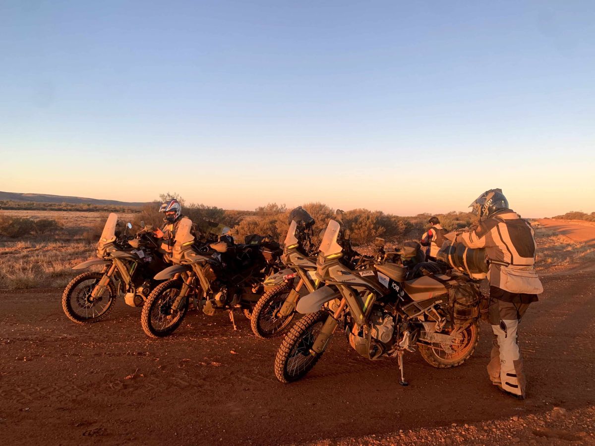 Four adventure motorcycles parked on a dirt roadside at sunrise during the Kicking Cancer's Ass Across Australia ride.