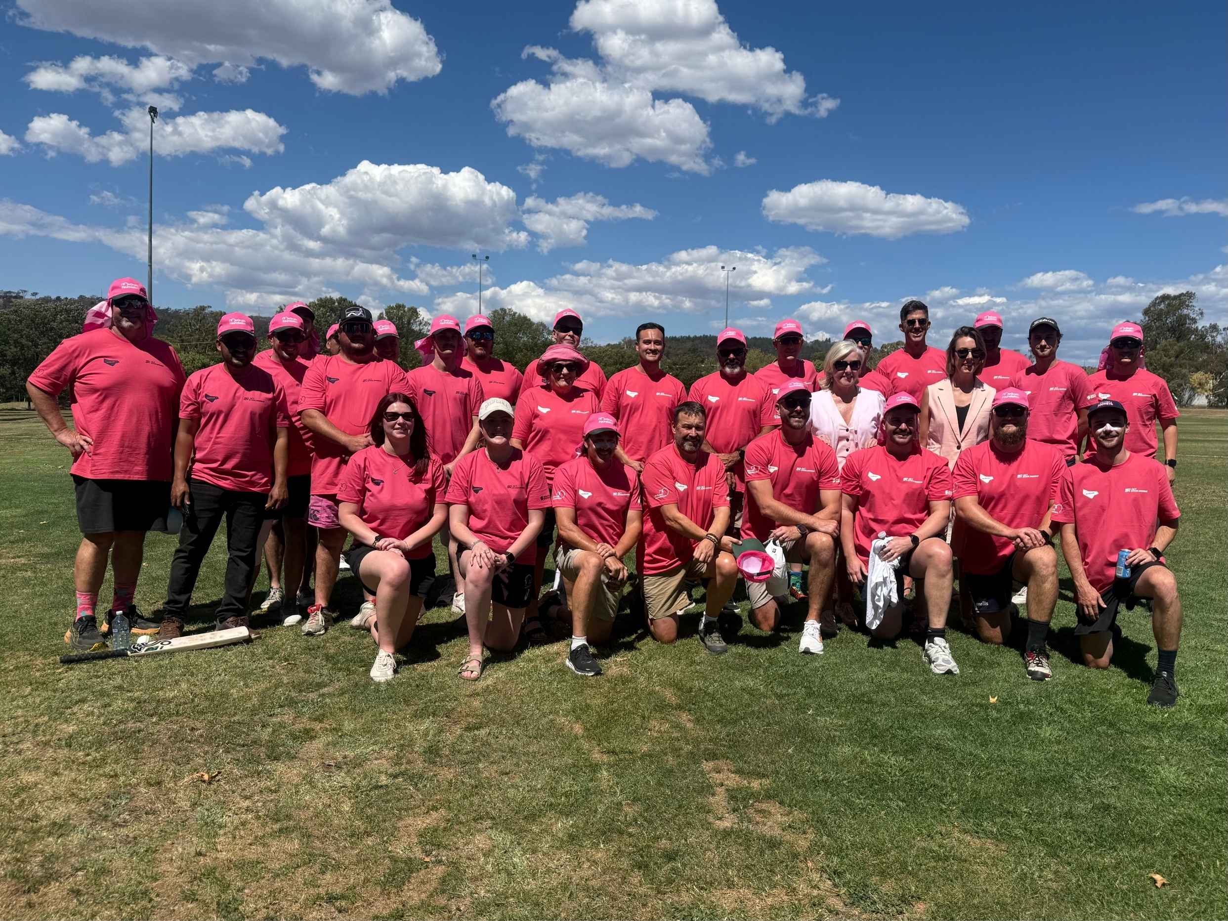 Group of Pink Stumps Day participants wearing matching pink shirts pose for a photo on a cricket field.